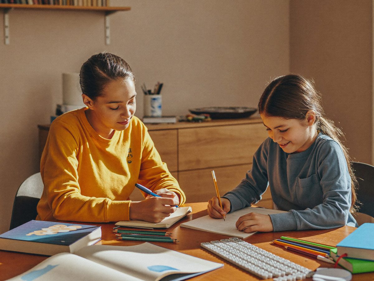 Educational therapist helping a school-age girl with reading and writing at a desk