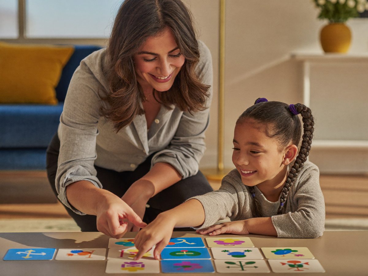 Speech therapist working at eye level with a young girl using picture communication cards